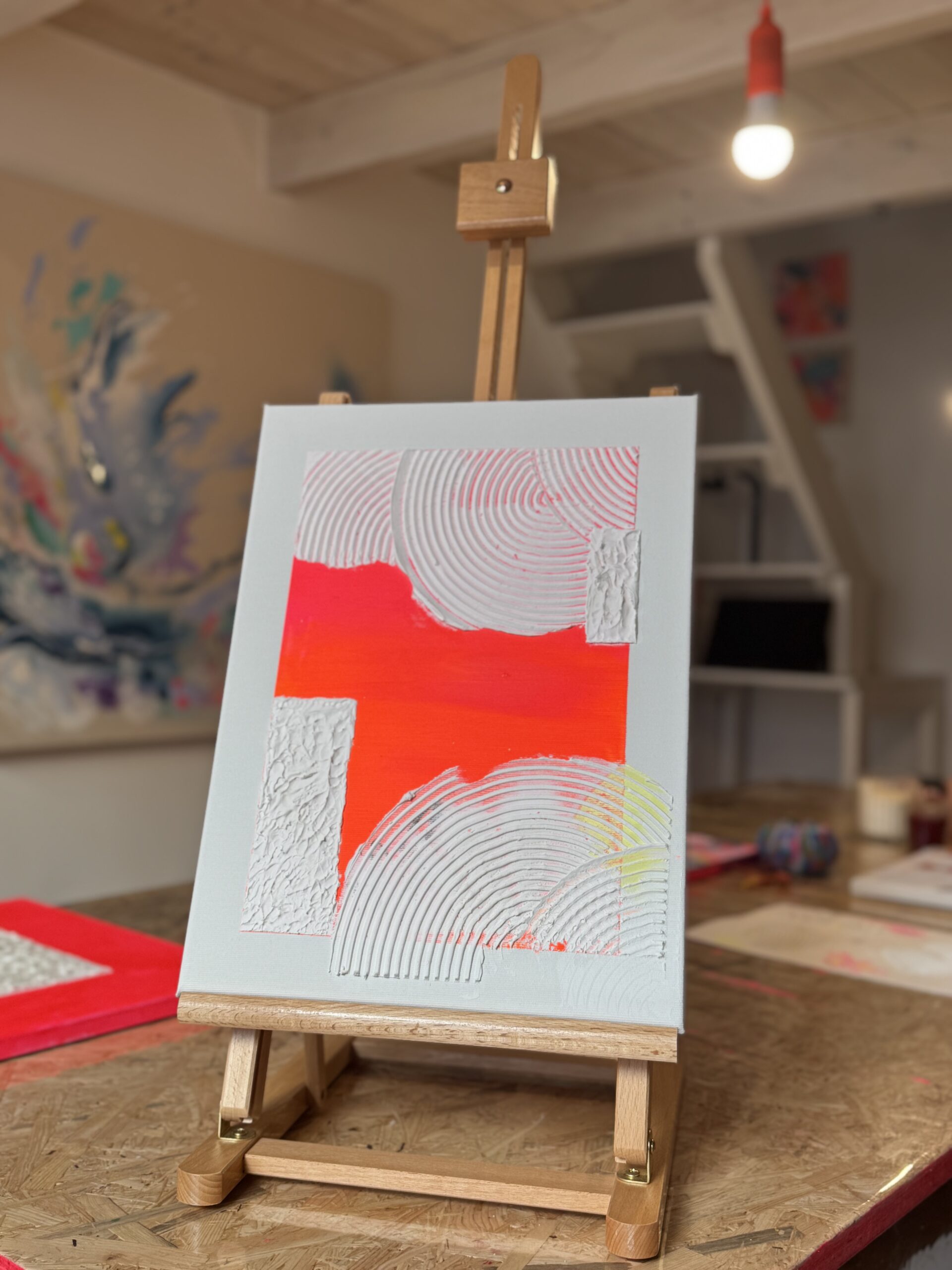 Abstraktes Bild in Hellblau mit leuchtend roten Farbflächen auf einer Staffelei im Atelier