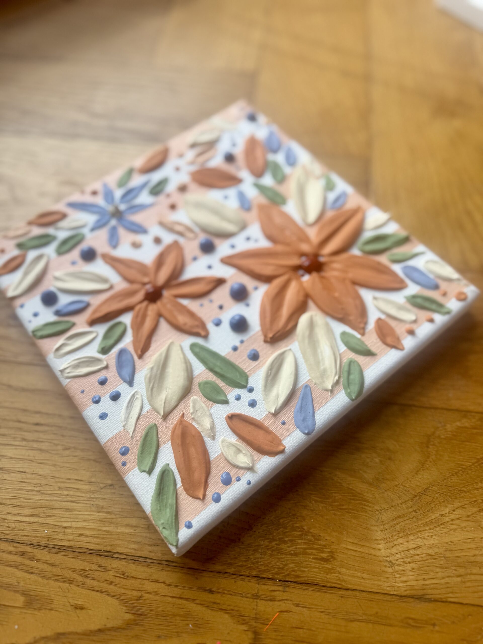 Kleine Leinwand mit gemalten Blumen in Terrakotta, Orange und Blau auf Holzboden