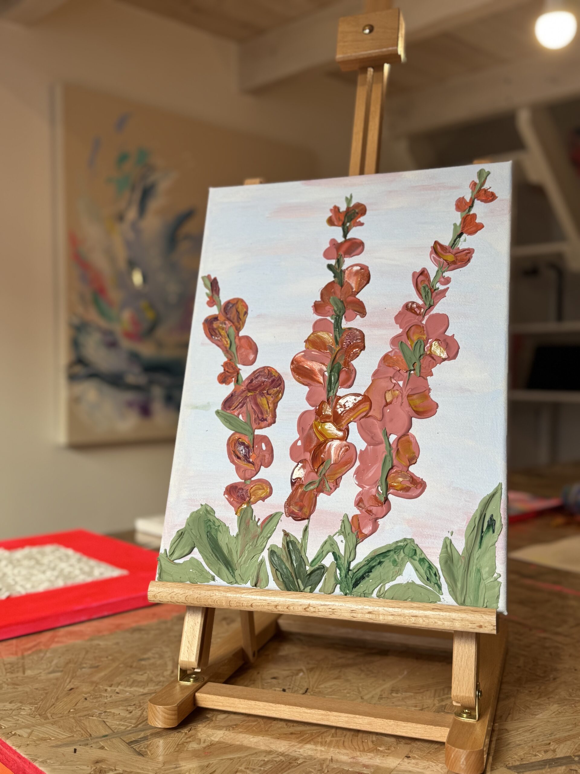 Leinwand mit gemalten rosa Blüten an grünen Stängeln auf einer kleinen Holzstaffelei