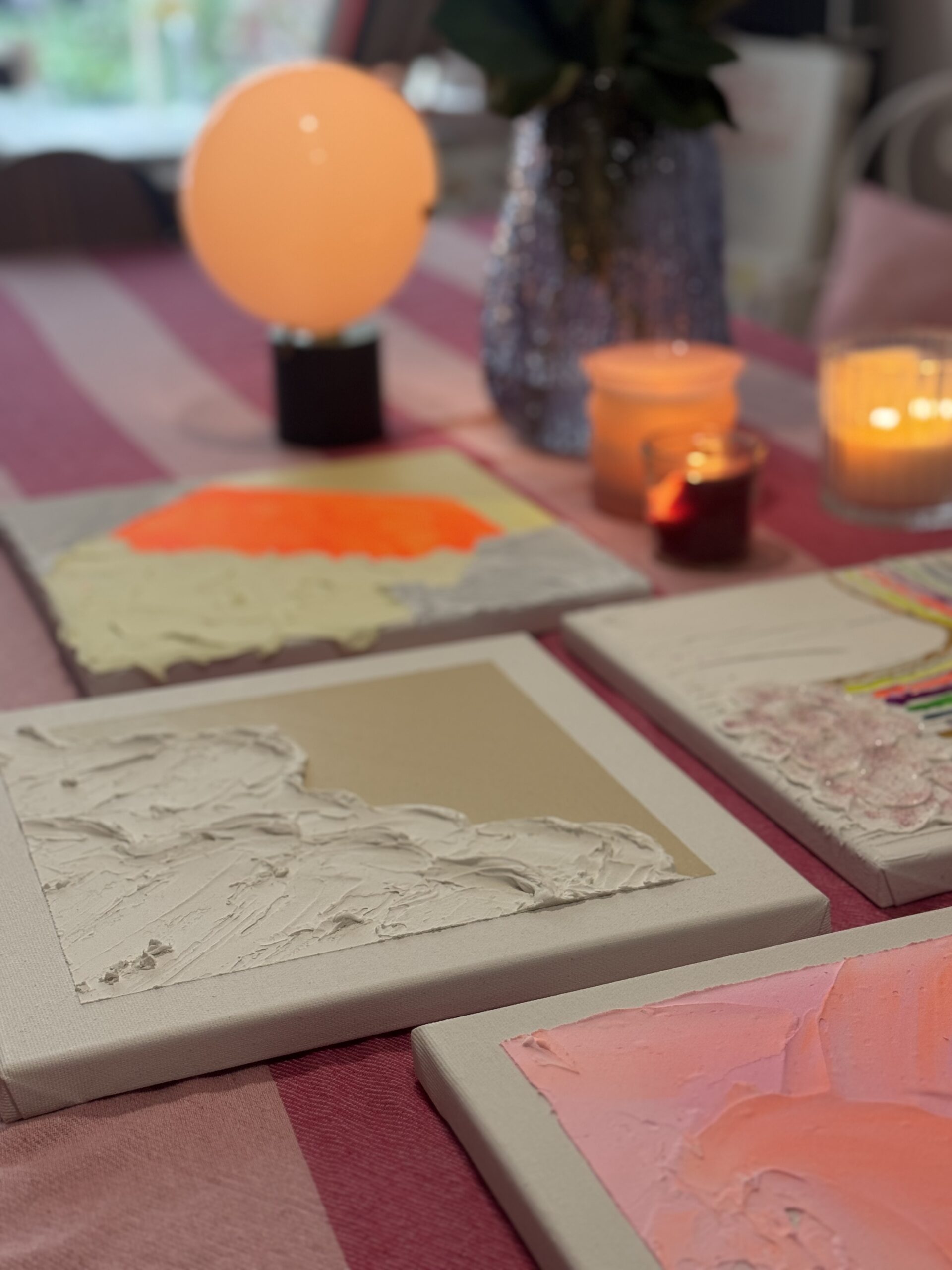 Workshop-Tisch mit strukturierten Leinwänden, Kerzen und einer leuchtenden orangefarbenen Kugellampe