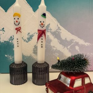 Bemalte weiße Kerzen mit winterlichen Motiven, daneben ein kleines rotes Spielzeugauto als Dekoration