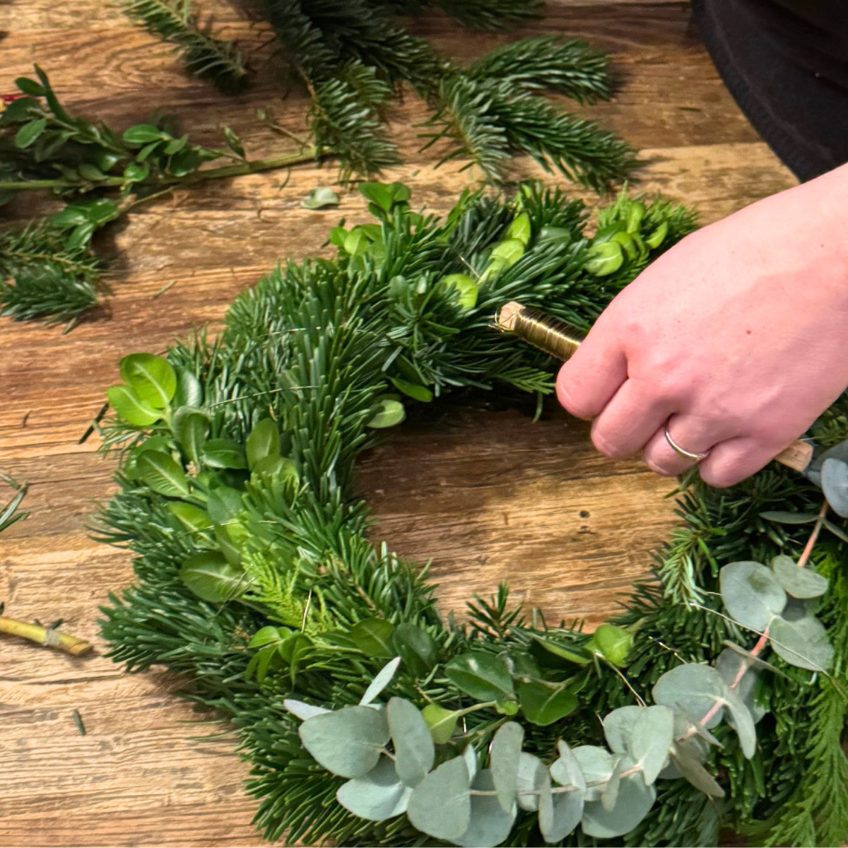 Hände arbeiten Tannen- und Eukalyptuszweige in einen Adventskranz ein